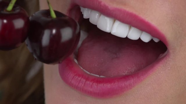 Slow motion close up: The young girl bites a cherry. Minimally invasive porcelain veneers/ smile/ porcelain veneers color bleach 1