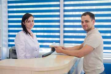 Mid adult female receptionist receiving card from patient in dentist clinic