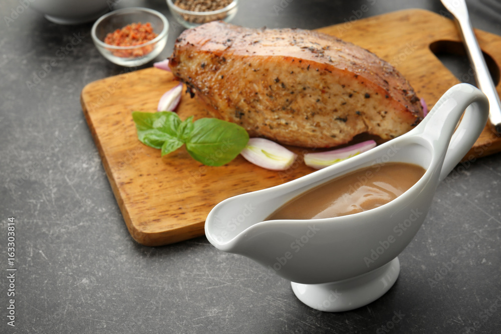 Wall mural tasty turkey gravy in sauce boat and cutting board with baked meat on table