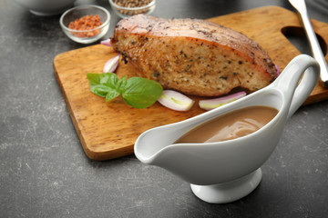 Tasty turkey gravy in sauce boat and cutting board with baked meat on table