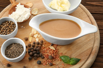Tasty turkey gravy in sauce boat and spices on wooden board