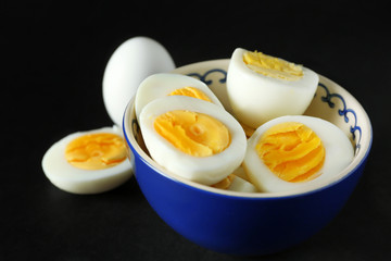 Bowl with sliced hard boiled eggs on black background. Nutrition concept