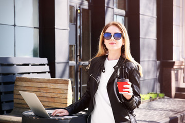Young girl holding cup of coffee and using laptop outdoors