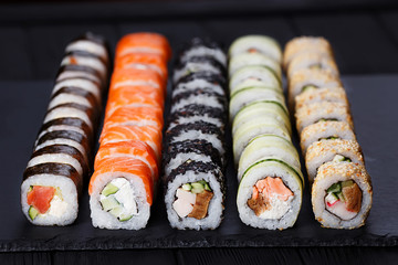 Japanese assorted tasty fresh sushi set served on black slate, close up. Food art, many delicious colorful rolls. Restaurant menu photo.