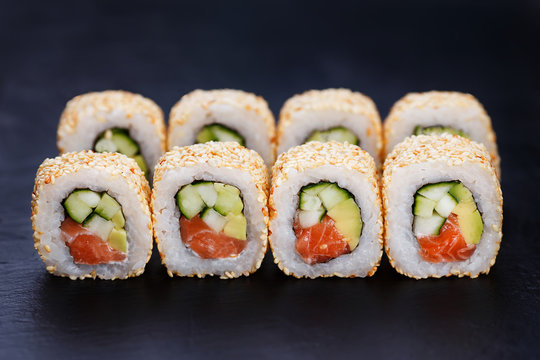 Appetizing fresh california sushi roll set with salmon in sesame served on black slate, close up. Japanese healthy seafood.