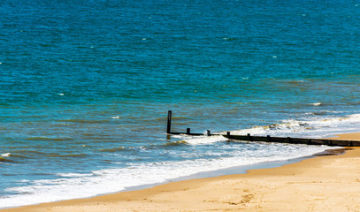 Dock pilings on a sandy beach, blue ocean and yellow sand, sunny hot day in seaside resort