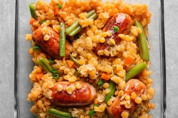 Glass bowl with tasty lentil porridge, sausages and vegetables on kitchen table, closeup