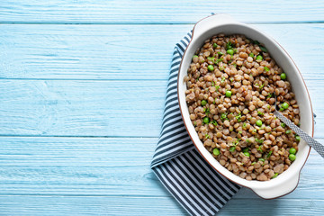 Casserole dish with tasty lentil porridge, spoon and napkin on light wooden table