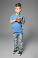 Cute little boy drinking juice on grey background