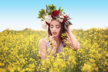Naklejka na ściany i meble Beautiful young woman wearing floral wreath in green field