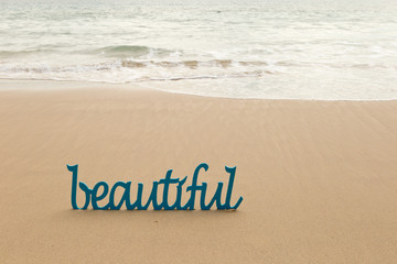 Beautiful - blue wooden word in sand with waves on beach