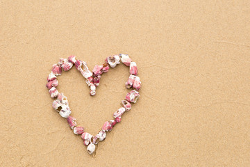 Heart shape in pink sea shells on beach