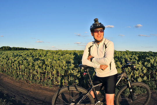 smiling cyclist with a bike in a field looking at the sunlight.