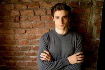 Obraz premium Portrait of a casually dressed young businessman standing with his arms crossed against a brick
