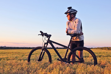 the cyclist with the bike in a field watching the sunset.