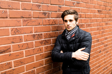 Cool fashion man sitting with his hand in pocket smiling and looking against brick wall