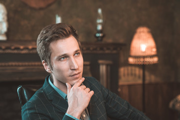 Portrait of a business man who sits by the fireplace with a thoughtful look...