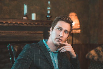 Portrait of a business man who sits by the fireplace with a thoughtful look...