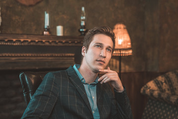 Portrait of a business man who sits by the fireplace with a thoughtful look...