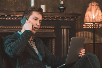 Man with computer sitting by the fireplace and talking on the phone