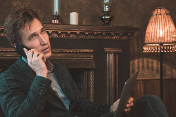 Man with computer sitting by the fireplace and talking on the phone