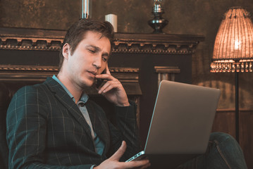 Man with computer sitting by the fireplace and talking on the phone