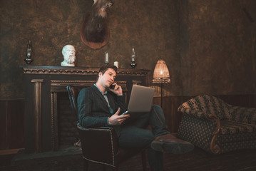 Man with computer sitting by the fireplace and talking on the phone