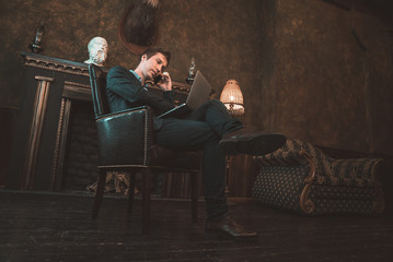 Man with computer sitting by the fireplace and talking on the phone