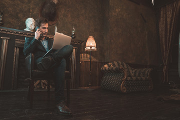 Man with computer sitting by the fireplace and talking on the phone