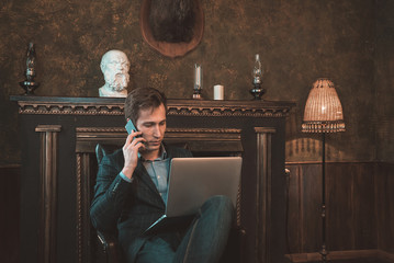 Man with computer sitting by the fireplace and talking on the phone
