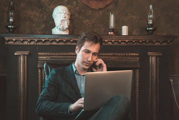 Man with computer sitting by the fireplace and talking on the phone