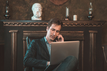 Man with computer sitting by the fireplace and talking on the phone