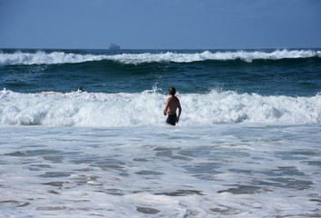 A guy is walking into the sea when big waves coming at high tide.