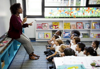Kindergarten students sitting on the floor listening to teacher - Powered by Adobe