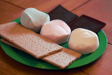 graham crackers, red, white and blue marshmallows, and chocolate bars on a green plate on a wood table
