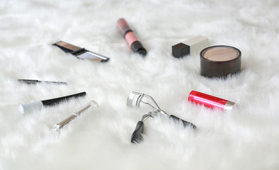 Different makeup cosmetics on white artificial fur background.