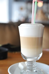 A cup of coffee stands on a brown table in a cafe. A cup of beautiful and fragrant latte with a slice of sugar - a refined sugar and tubules is on the table in a cafe. Cafe inside with visitors and la