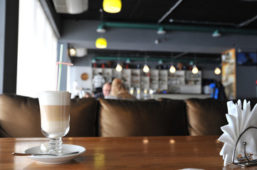 A cup of coffee stands on a brown table in a cafe. A cup of beautiful and fragrant latte with a slice of sugar - a refined sugar and tubules is on the table in a cafe. Cafe inside with visitors and la