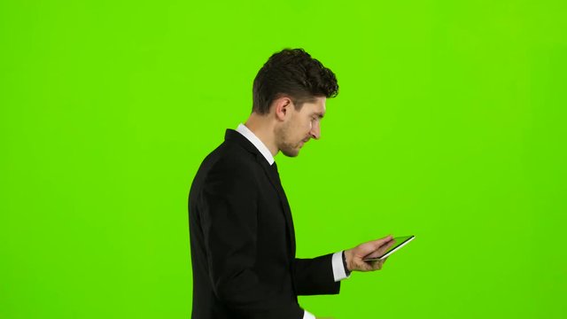 Businessman walks, thumbs a notebook, and makes a selfie. Green screen. Side view