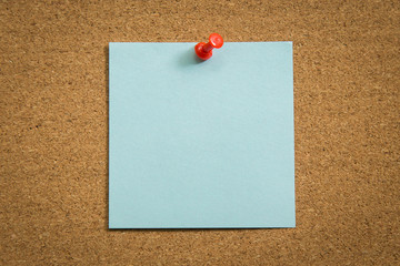 Blank note paper with a red push pin on cork board.