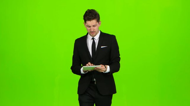 Businessman walks, thumbs a notebook, and makes a selfie. Green screen