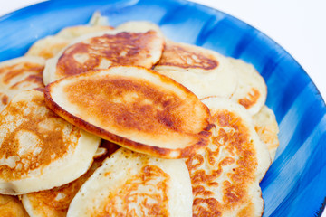 Ruddy freshly cooked pancakes lie on a blue plate on a white background.