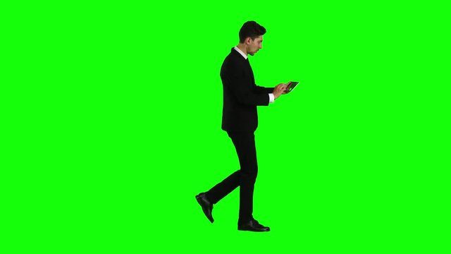 Businessman walks, thumbs a notebook, and makes a selfie. Green screen. Side view