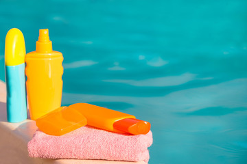 Cream for safe tanning on blue water background and pink towel