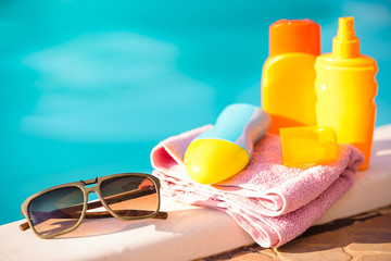 Set for rest: Cream for tanning, sunglasses, towel on blue water background and pink towel