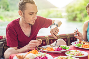 Young man eats vegetables and fish outdoors in a cozy restaurant on the water, discover new kitchen