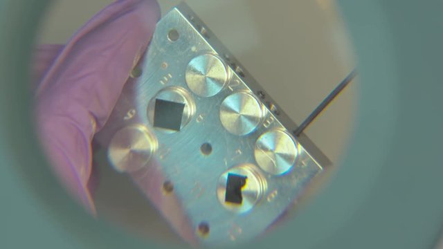 Unscrewing parts of a electron microscope sample table looking through a magnification glass. Working on a electron microscope.