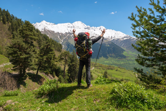 Joyful man traveler with open arms stands on the alpine meadow