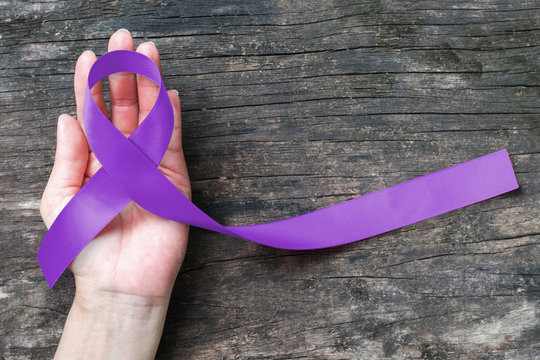 Hodgkin's lymphoma and testicular cancer awareness violet ribbon symbolic bow color on helping hand support and aged wood (isolated with clipping path)