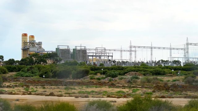 Electricity power station in remote industrial area and high voltage power lines, taken through out of focus barbed wire fence, 4k handheld panning.